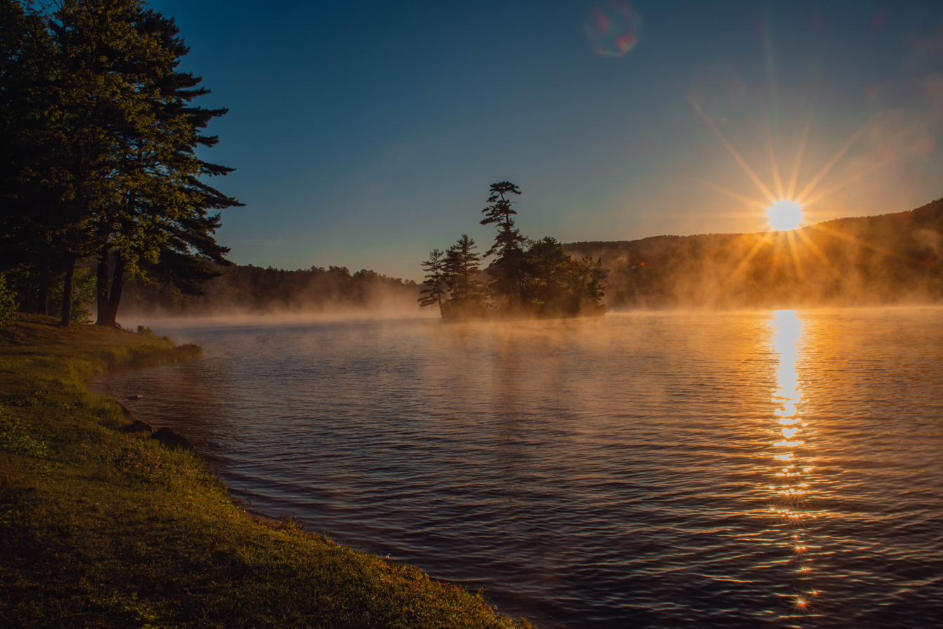 Sunrise over a misted lake, light raking across the water